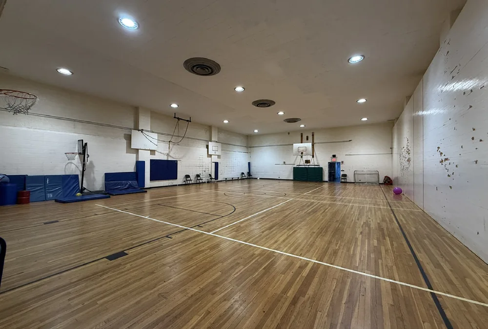 The indoor gymnasium at the school building, with basketball hoops and a wood court