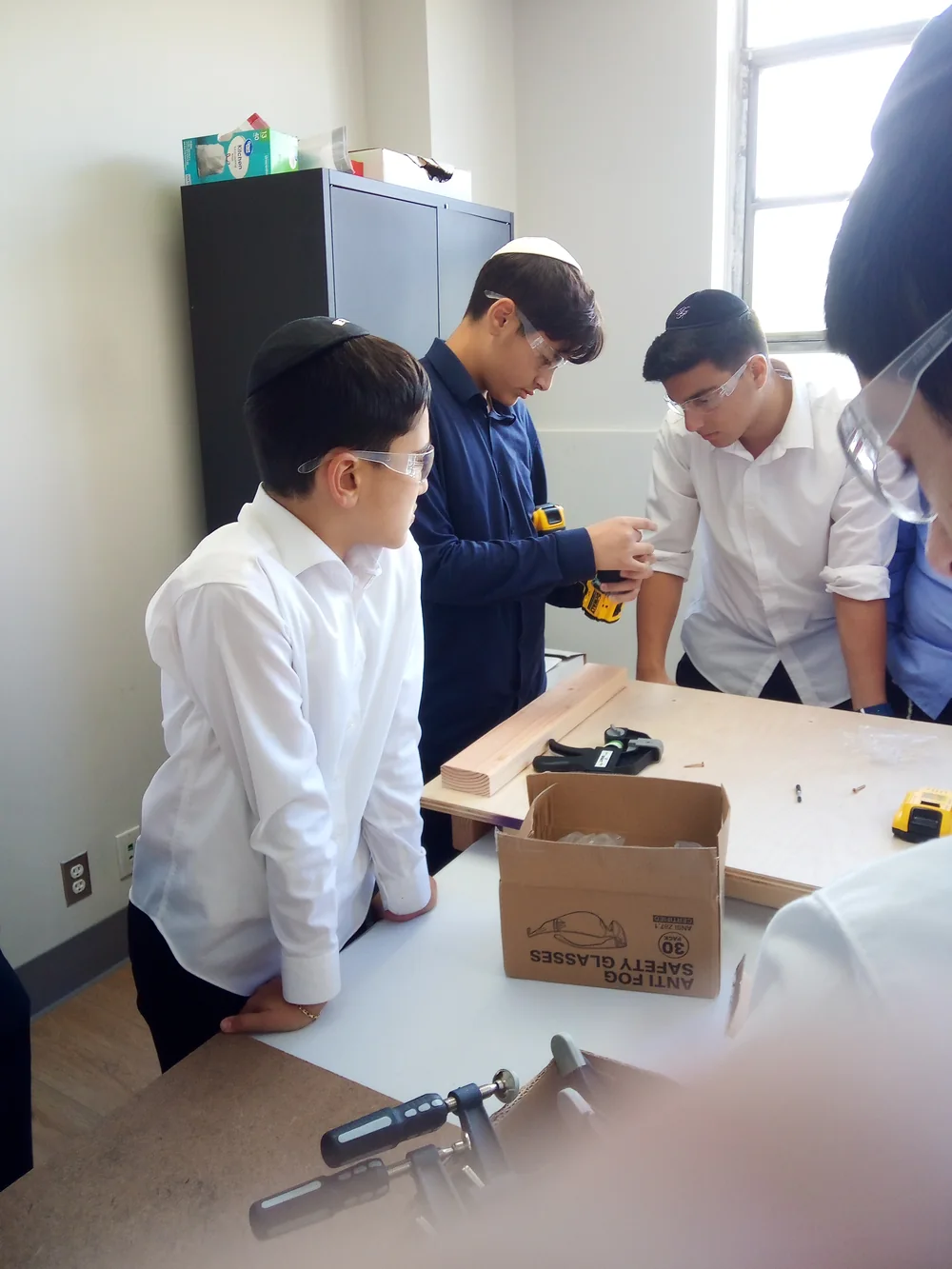 Students wearing safety glasses work together on a woodworking project